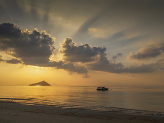seaside of small boat floating in the sea with small island and sun rays with yellow sun light and cloudy sky background, sunrise at Ko Bulon Le, Stun Province, southern of Thailand.