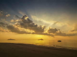 seaside of small boat floating in the sea with small island and sun rays with yellow sun light and cloudy sky background, sunrise at Ko Bulon Le, Stun Province, southern of Thailand.