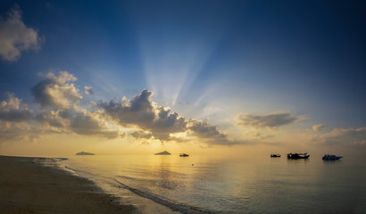 view panorama seaside of small boat floating in the sea with small island and sun rays with yellow sun light and cloudy sky background, sunrise at Ko Bulon Le, Stun Province, southern of Thailand.