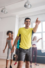 Selective focus of trainer and multiethnic dancers pointing with finger while dancing zumba in studio
