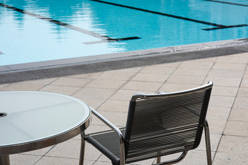 Relaxing chair and circle glass table near a swimming pool in a sport club with a relaxing atmosphere waiting for someone to sit on. Holidays, long vacations or short break.