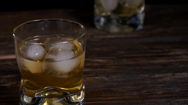 Ice cubes fall into a glass with golden malt whiskey 