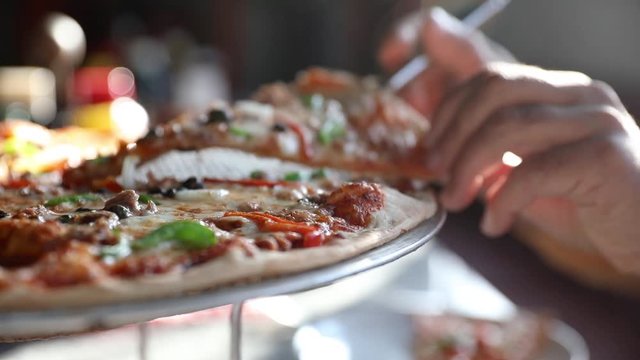 Closer-up Hands of a man taking a slice of hot steaming tasty seafood pizza with capers and olives served on a round pizza stand on a plate. HD slow motion video 1920X1080