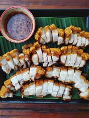 Thai roasted crispy pork on banana leaf with Thai Spicy Sauce, on wooden cutting board, Close up view