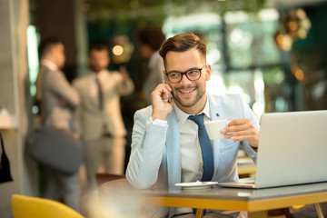 Young business man talking mobile phone and drinking coffee