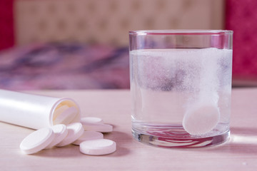The effervescent tablet dissolves in a glass of water. A handful of pills on the table. Blurred...