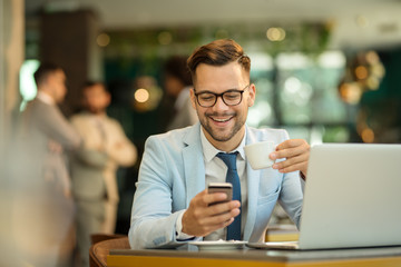 Happy young business man sitting at cafeteria with laptop and mobile. Businessman typing on smart phone while sitting in a pub restaurant.