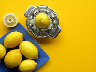 ripe lemons in a blue plate and a manual steel juicer on a yellow background