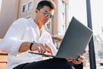 young stylish guy in shirt with phone and notebook on bench on sunny warm day outdoors, freelance