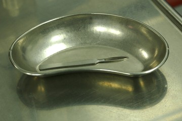 Metal tray, scalpel and medical glove on metal table in medical office
