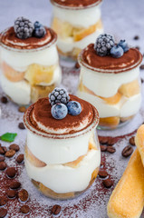 Gourmet Italian tiramisu dessert in a glass sprinkled with cocoa and decorated frozen berries. Vertical orientation. Close up