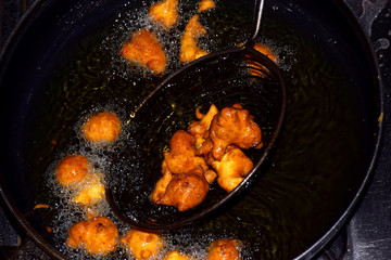 gram flour fritters, boiling oil in frying pan with dark background