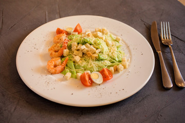 Close up view of the Caesar salad with shrimps on the white plate on the grey background.