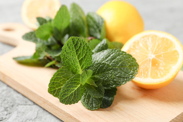 Cutting board with lemon and mint on grey background, close up