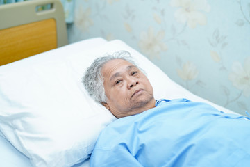 Asian senior or elderly old lady woman patient smile bright face with strong health while lying on bed in nursing hospital ward : healthy strong medical concept .