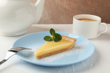 Plate with lemon tart slice, teapot and cup of tea on white table, close up