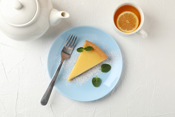 Plate with lemon tart slice, teapot and cup of tea on white background, top view
