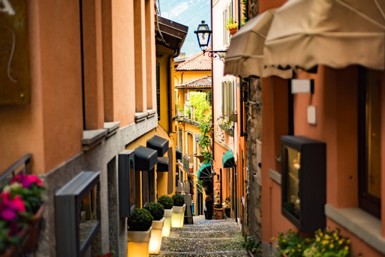Narrow street with orange buildings and lanterns in Bellagio town at the famous Italian lake Como, Lombardy, North Italy with stone steps and Alps mountains on background.