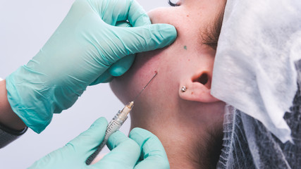 The female beautician doctor making injection in young woman face. The doctor cosmetologist doing facial contouring procedure.