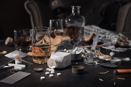 Various drugs, alcohol and cigarettes are on the wooden table. Substances that cause drug and alcohol dependence. Low key.