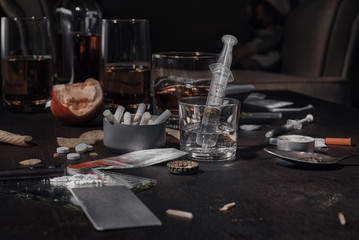 Various drugs, alcohol and cigarettes are on the wooden table. Substances that cause drug and alcohol dependence. Low key.
