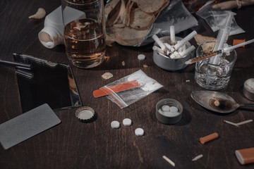 Various drugs, alcohol and cigarettes are on the wooden table. Substances that cause drug and alcohol dependence. Low key.