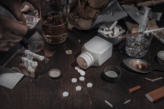 Various drugs, alcohol and cigarettes are on the wooden table. Substances that cause drug and alcohol dependence. Low key.