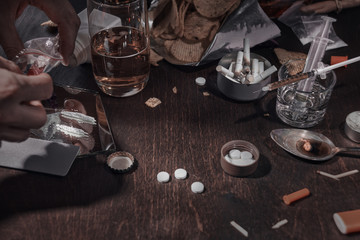 Various drugs, alcohol and cigarettes are on the wooden table. Substances that cause drug and alcohol dependence. Low key.