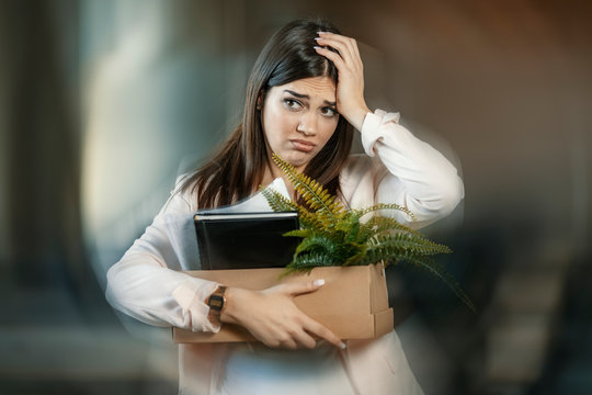 Losing job. Sad quiet young woman looking calm and frustrated while coming home with a heavy box full of personal items after losing her job. Office lady in workplace seeking job