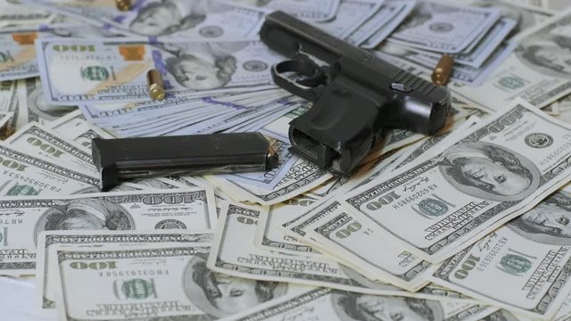 A lot of real dollars bills and black gun on the table. Money and weapons. Gun against the dollar bills.