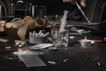 Fototapeta na wymiar Various drugs, alcohol and cigarettes are on the wooden table. Substances that cause drug and alcohol dependence. Low key.