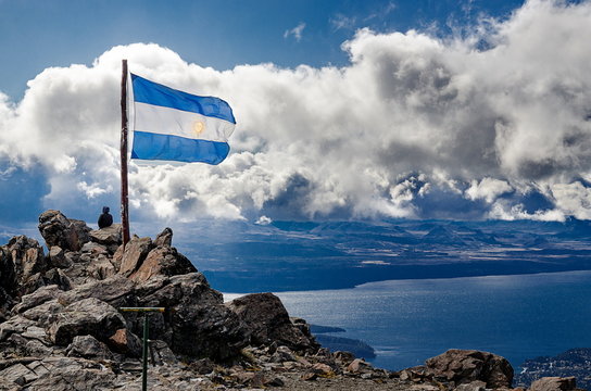 Argentinian Flag On Mountain With Lake In Background Against Cloudy Sky