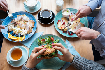 Colorful breakfast on wooden table with hands of people. Various food and different meal during the family breakfast in the morning. Flat lay and top view.