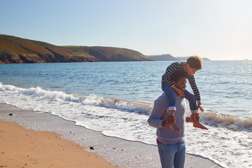 Loving Father Giving Son Ride On Shoulders As They Walk Along Beach Together