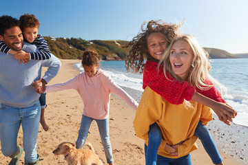 Parents Giving Children Piggybacks As They Walk Along Winter Beach Together