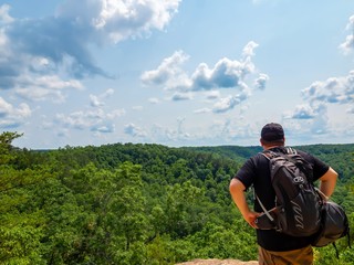 Man, hiker, standing on top of the Natural Bridge in Kentucky looking out into the sky filled with...