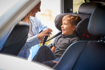 Mother Securing Son Into Rear Child Seat Before Car Journey
