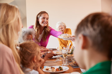 Mother Serving Food As Multi-Generation Family Meet For Meal At Home