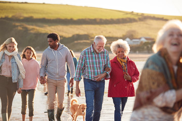 Active Multi-Generation Family With Dog Walking Along Shore On Winter Beach Vacation
