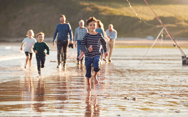 Children Run Ahead As  Multi-Generation Family Walk Along Shore On Winter Beach Vacation