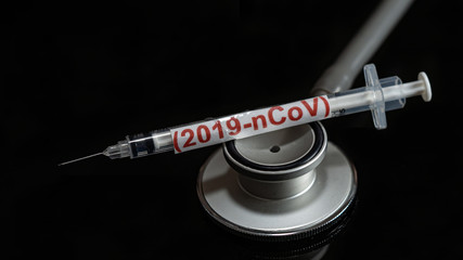 syringe have text "(2019-nCoV)  with Medical stethoscope  put on  Black background. corona virus Concept.