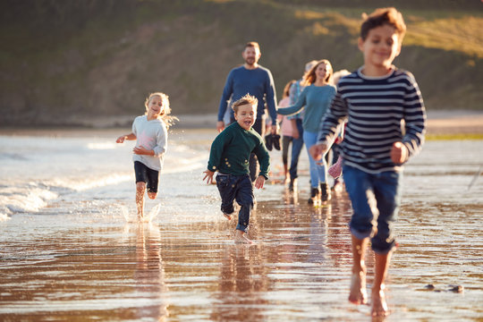 Children Run Ahead As  Multi-Generation Family Walk Along Shore On Winter Beach Vacation - Powered by Adobe