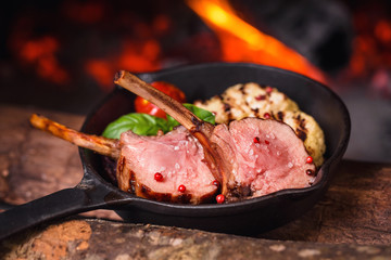  two juicy pieces of rack of lamb in a pan on a background of fire from the oven