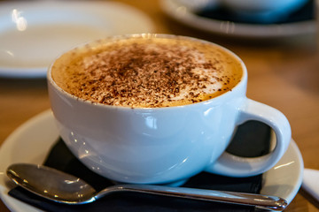 White cup with cappuccino coffee with cinnamon or cacao powder