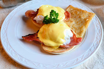 Weekend brunch in Scotland with two eggs benedict on homemade muffuns with roasted bacon and yellow hollandaise sauce.