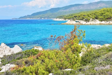 Naklejka premium Seascape of rocky beach with blurred azure sea water in sunny day. Amazing natural beach with white stones and turquoise water. crystal clear sea with sun reflection. Halkidiki Greece Blue Flag Beach