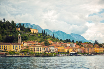 Fototapeta na wymiar Amazing view of Como Lake and Bellagio, panorama of lake with small town and Alps mountains on background in cloudy day. Vacation on Como, Lombardy, Italy. Popular tourist destination. Italian city.
