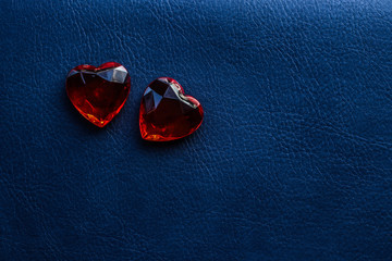 Two red faceted glass hearts on a blue leather horizontal background with free space