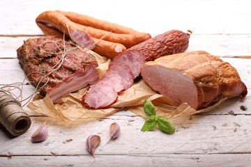 Composition of aromatic, smoked cold cuts on a white, wooden background. Traditional meat delicacies.