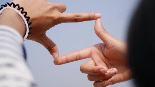 Young woman hands making frame shape sign on blue sky background slow motion.